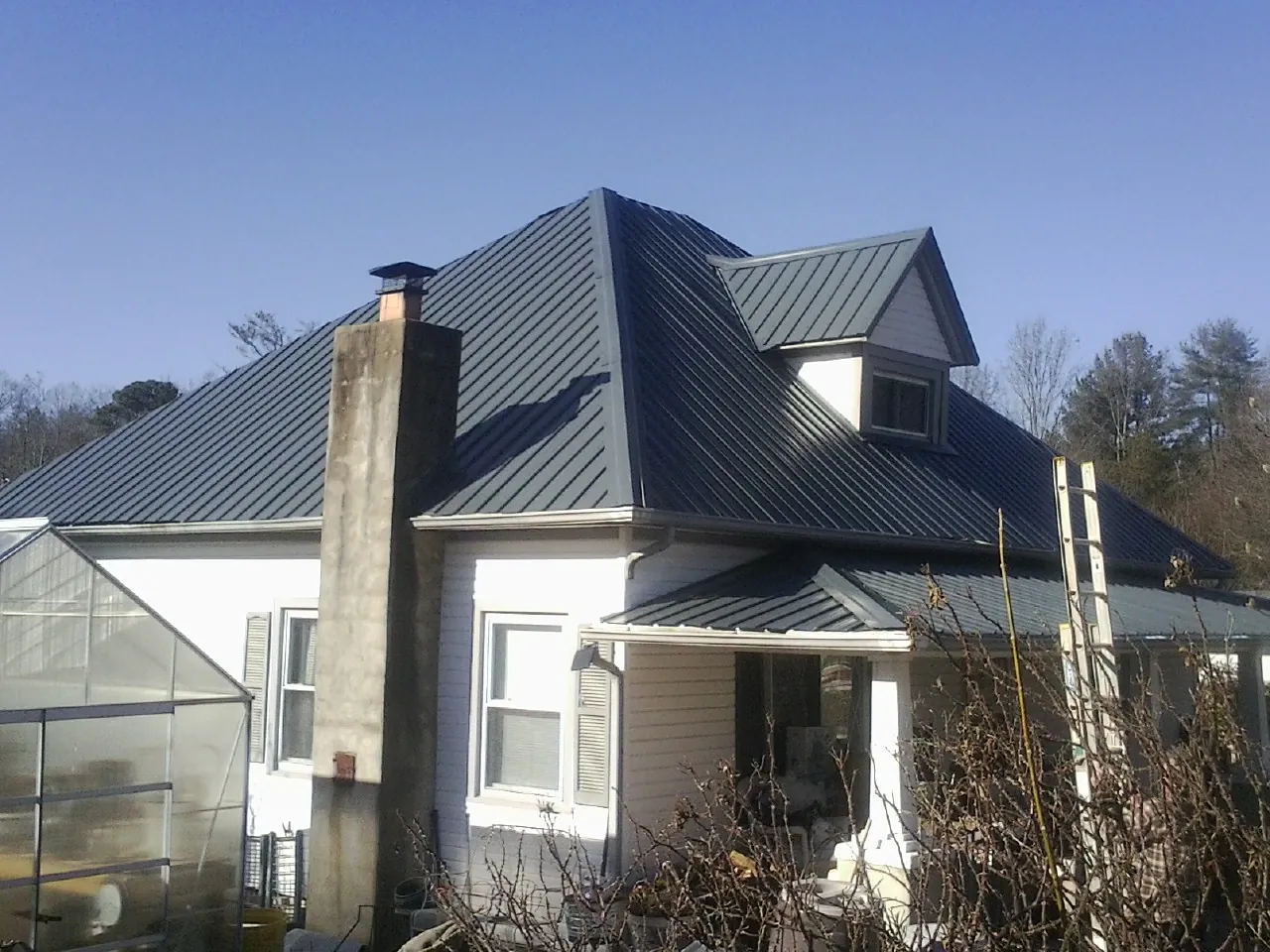 Dark blue standing seam metal roof on a white farmhouse with dormer — Slate & Tile Roof Repair by Roofing Brothers in Meredith
