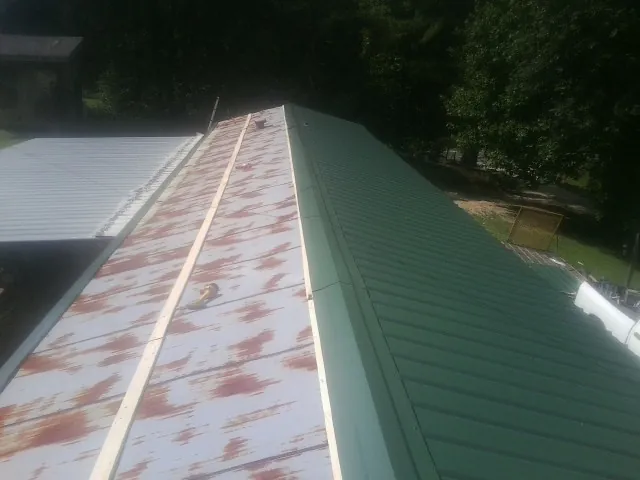 Old rusted panels beside newly installed green metal roofing — Wind Damage Roof Repair by Roofing Brothers in Meredith