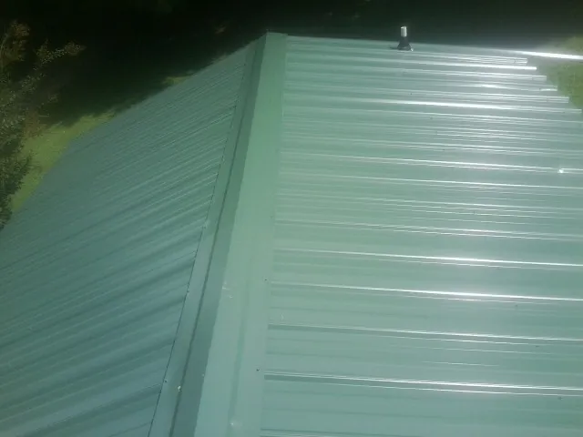 New green metal panels meeting at the ridge of a roof — Flat Roof Repair work by our crew in Meredith