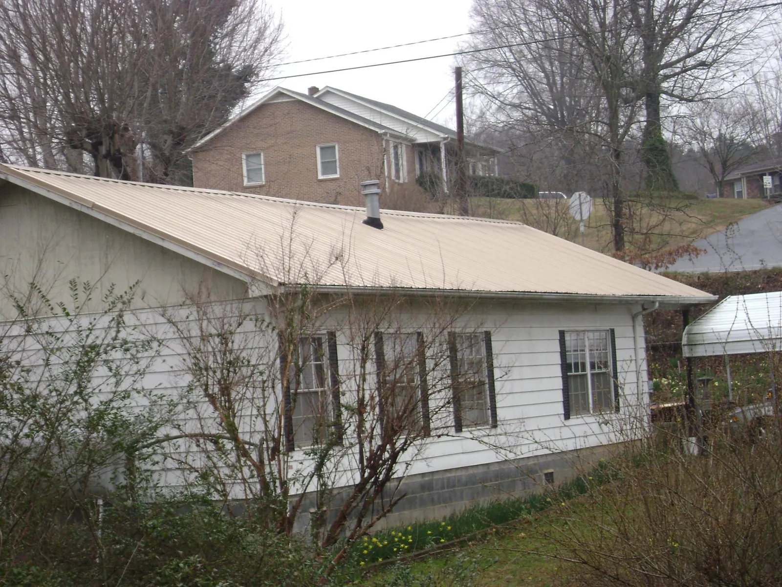 Tan metal roof on a white sided house set into a hillside — Commercial Roofing by Roofing Brothers in Meredith